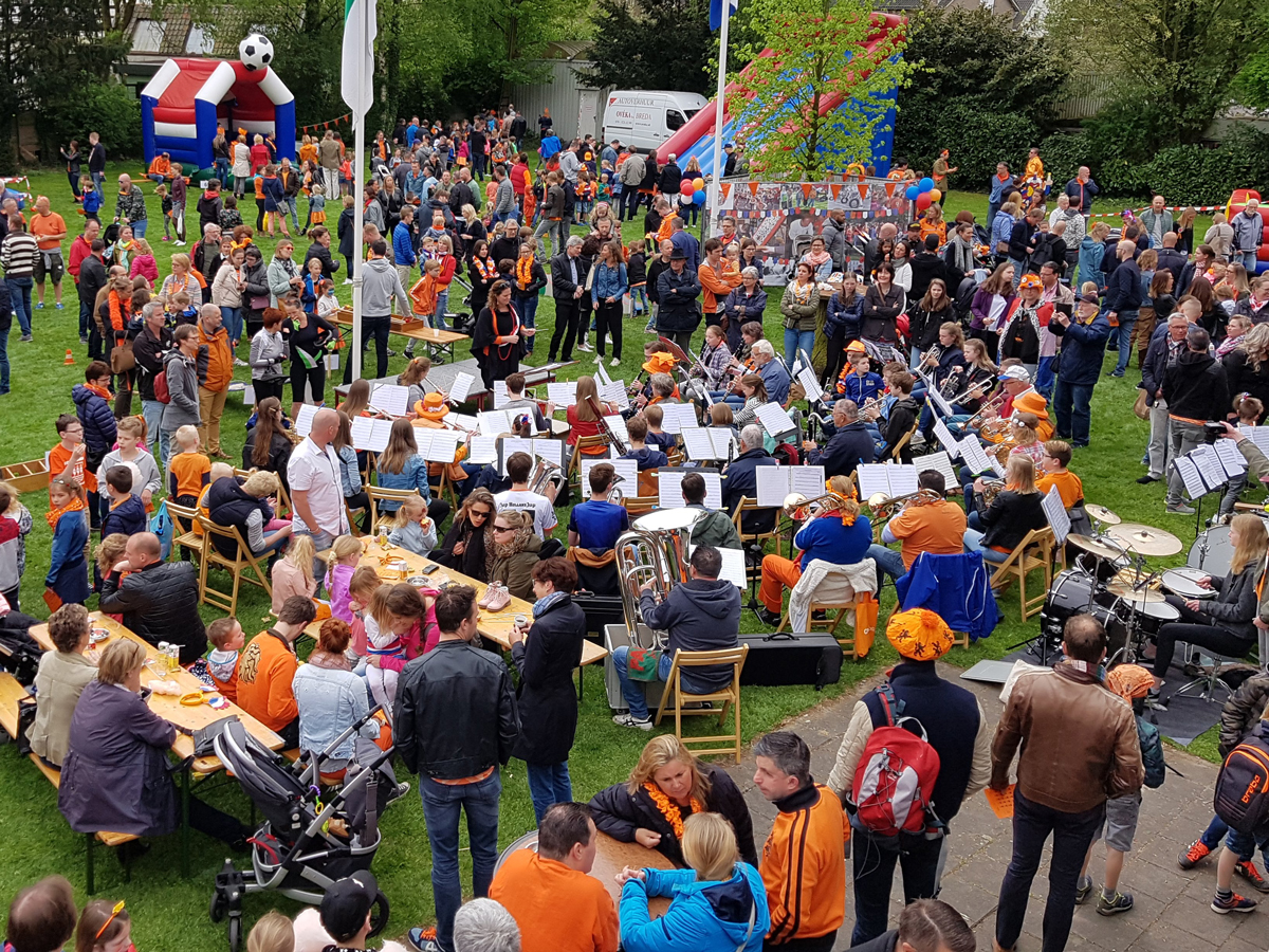 Dorspwei tijdens koningsdag. Een harmonie-orkest speelt voor publiek in oranje kleding