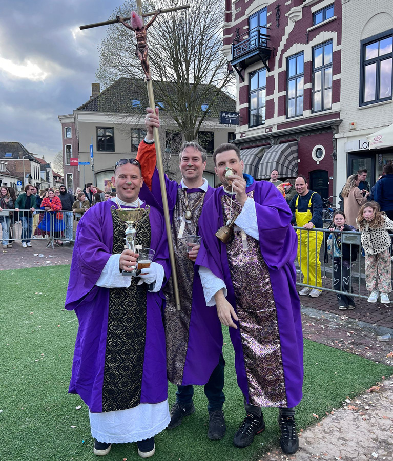 3 mannen verkleed als priesters in paars en witte jurken