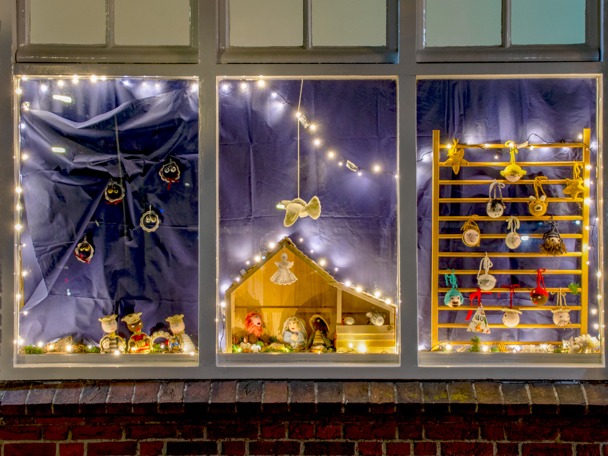 Kerstceratie van gehaakte kesrstal achter een raam