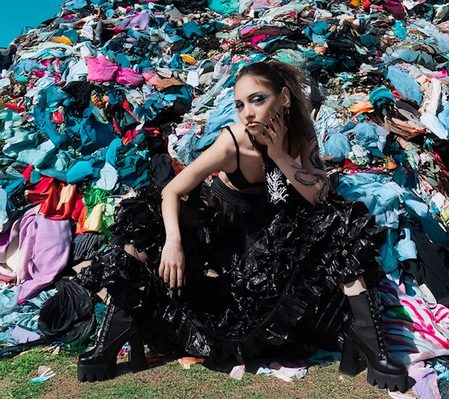 model zit voor een afvalberg van fast hashion kleding