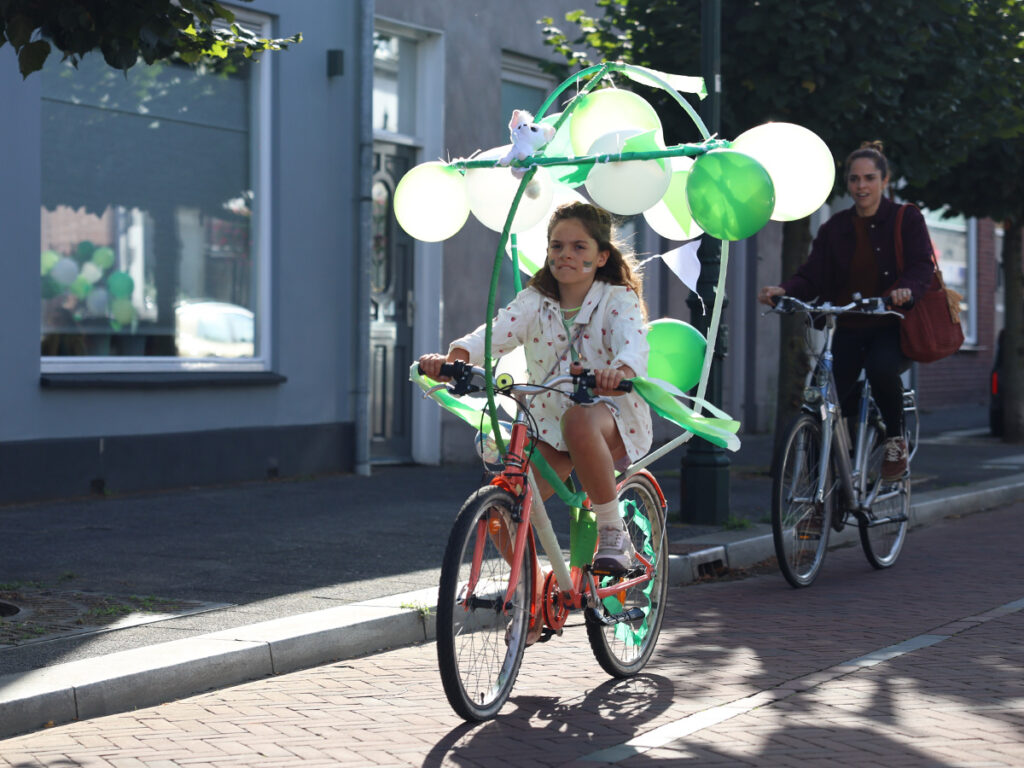 meisje op een versierde fiets met groen en witte ballonnen.