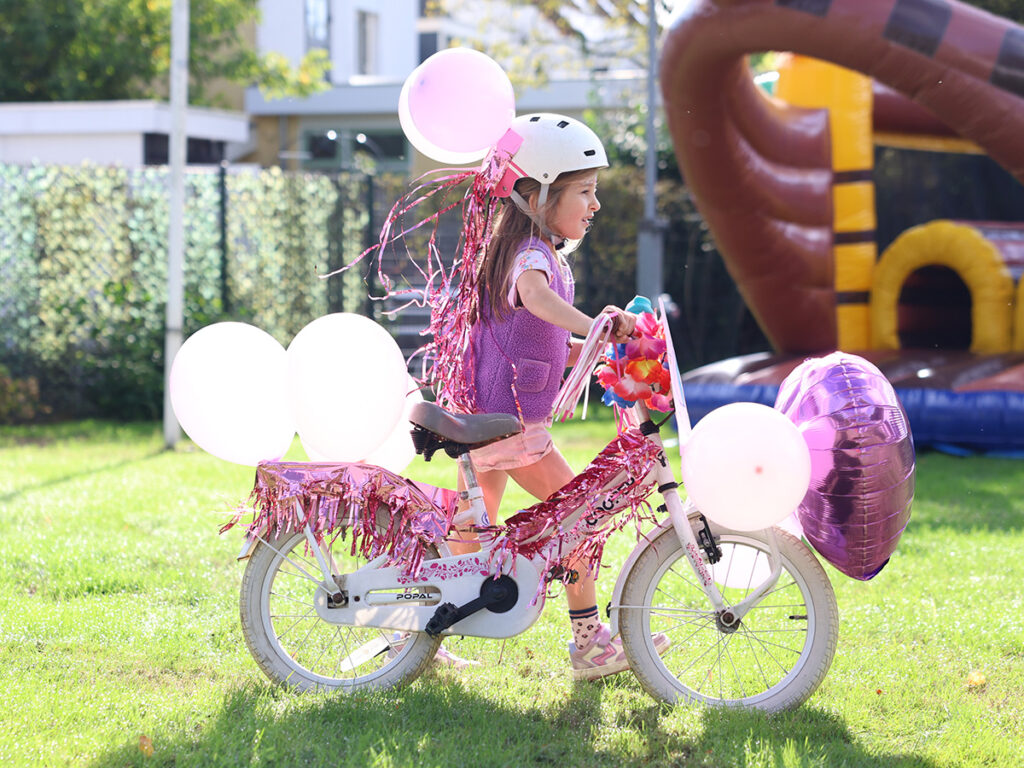 Een meisje met een mooi versierde fiets met veel roze en witte ballonnen.