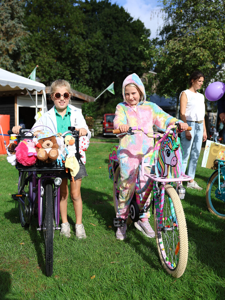Twee meisjes staan bij versierde fietsen waarvan een fiets versierd is met knuffels en de andere met een eenhoorn