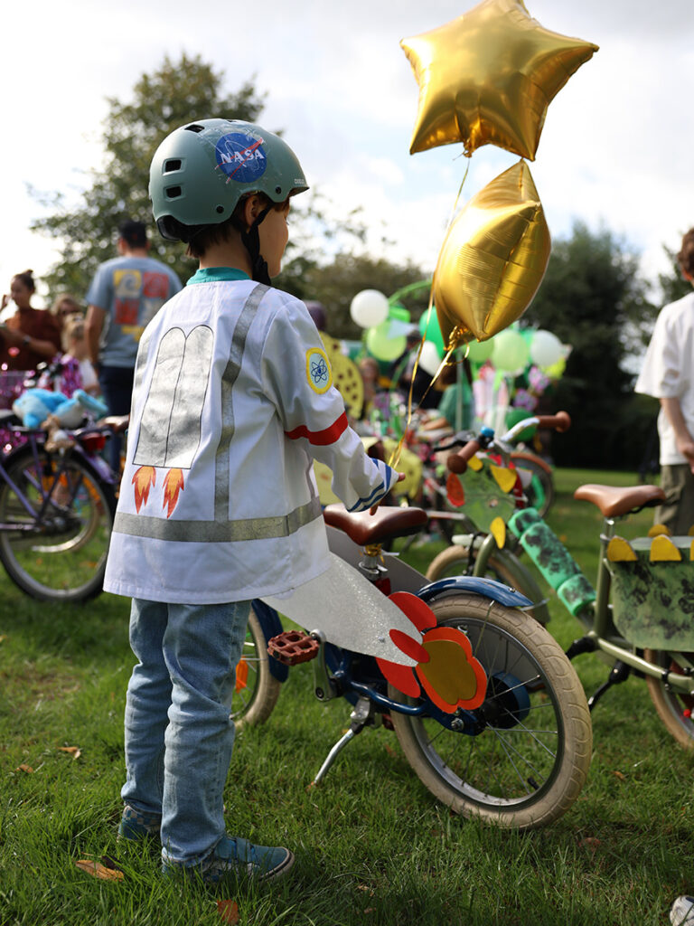 jongen met helm met een nasa-sticker, laat zijn de achterzijde van zijn hesje zien. Op het hesje staat een raket.
