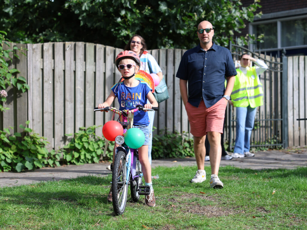 Twee ouders komen aangelopen met een meisje op een versierde fiets