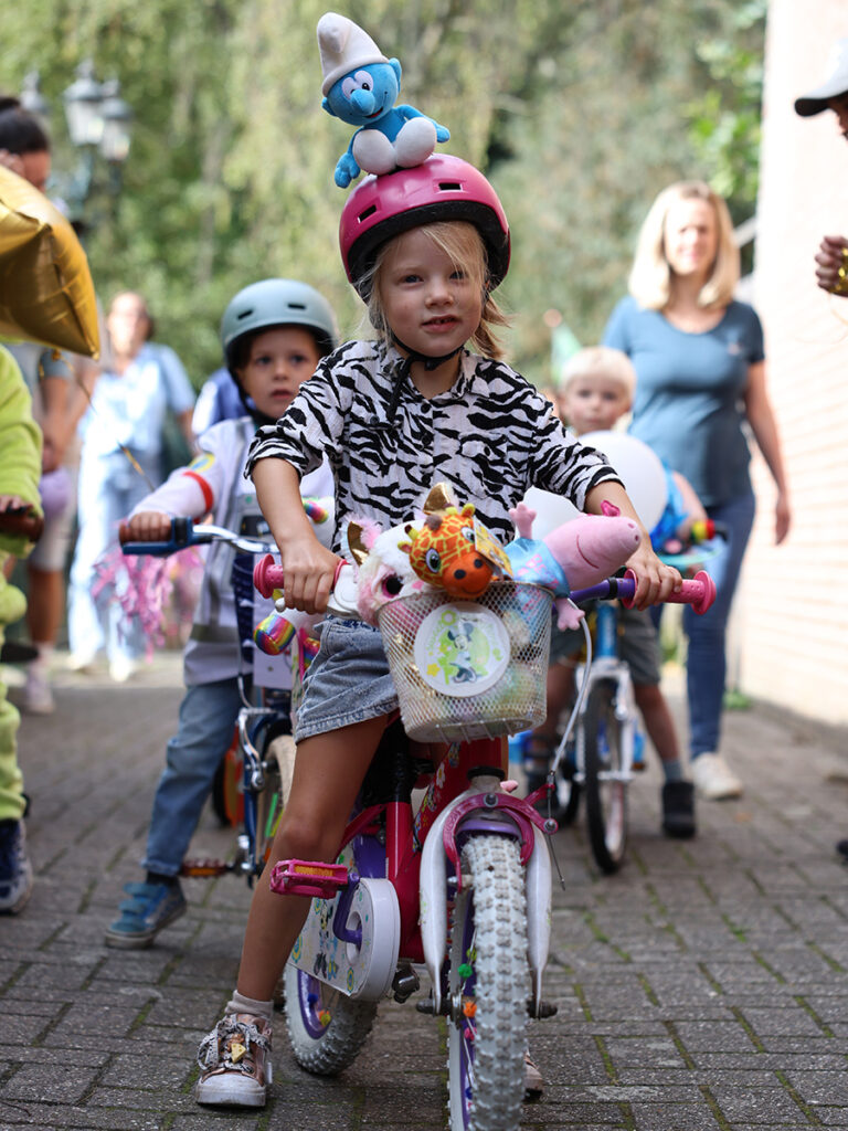 meisje heeft een bluwe smurf op haar helm heeft in haar fietsmand diverse knuffels