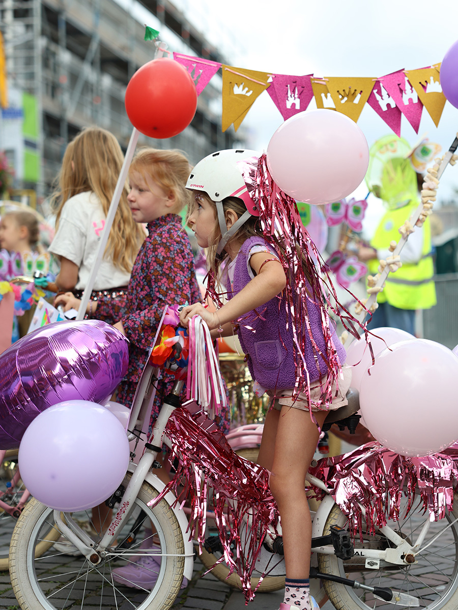 Meisje met een schitternd versierde fiets met veel ballonnen, glitters en franjes.