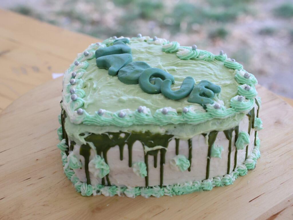 Een mintgroene taart in een hartvorm met daarop Aogje gespoten in botercreme