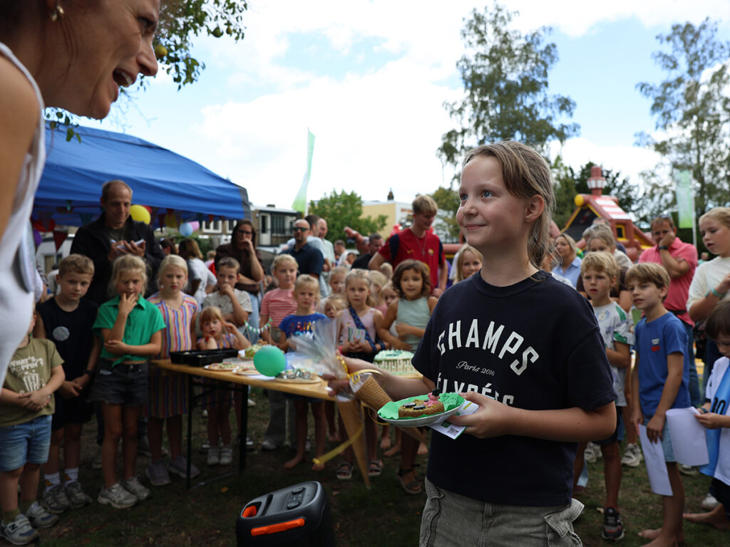 Meisje wordt gefeliciteerd door Margot terwijl een groep kinderen toekijkt.