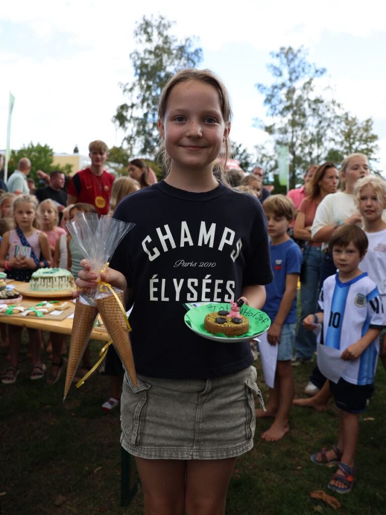 Meisje toont een groen bordje met een koekje. In haar andere hand heeft ze 2 ijshoorntjes vast.