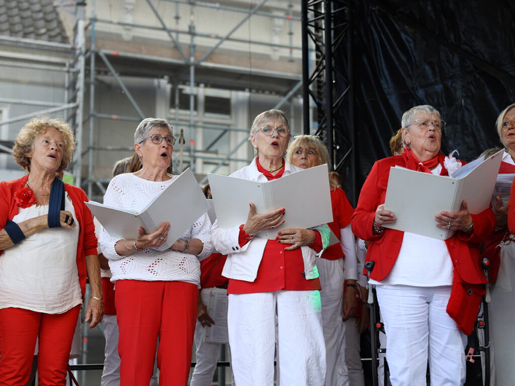 Vier dames gekleed in rood en wit zingen op het podium met een map met liederen
